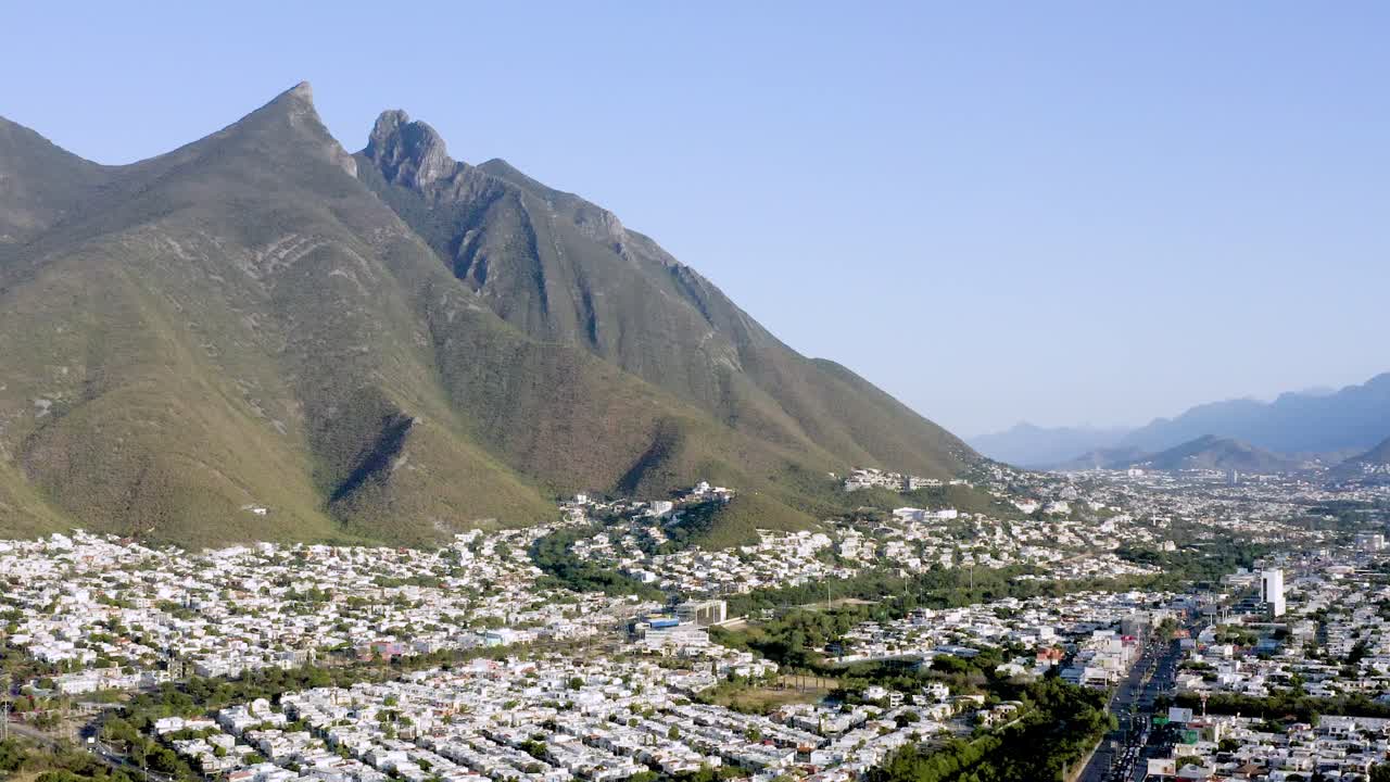 Filmato aereo panoramico realizzato con drone che cattura il Cerro de la Silla che sovrasta la campagna vicino a Monterrey, in Messico. Lo scatto evidenzia il contrasto tra l'iconica formazione montuosa e la zona rurale circostante