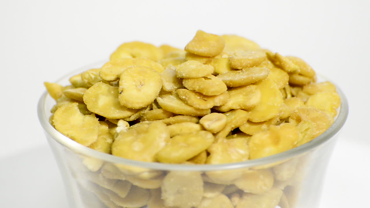 흰색 배경에 구운 파바 콩이 회전하는 투명한 유리 그릇