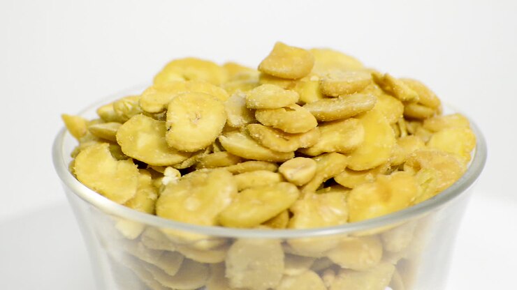 Ciotola di vetro trasparente con fave tostate in rotazione su sfondo bianco