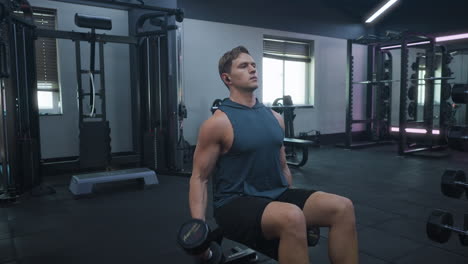hombre caucásico haciendo rizos de bíceps con pesadas pesas en un gimnasio oscuro