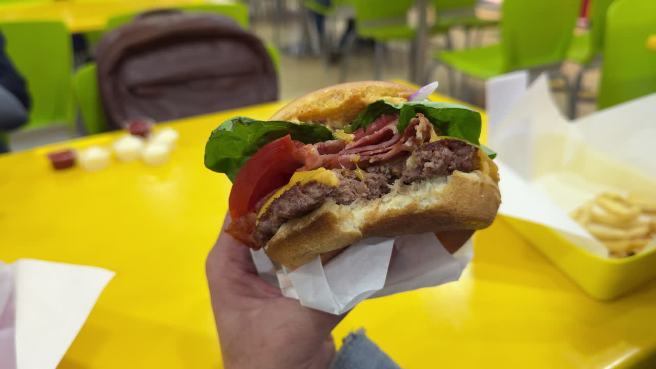 Close slow pan of a bitten bacon cheeseburger held by hand