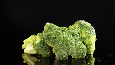 broccoli florets rotate smoothly on a glossy black surface, illuminated by studio lighting. the camera maintains a steady, close-up perspective, highlighting texture and freshness
