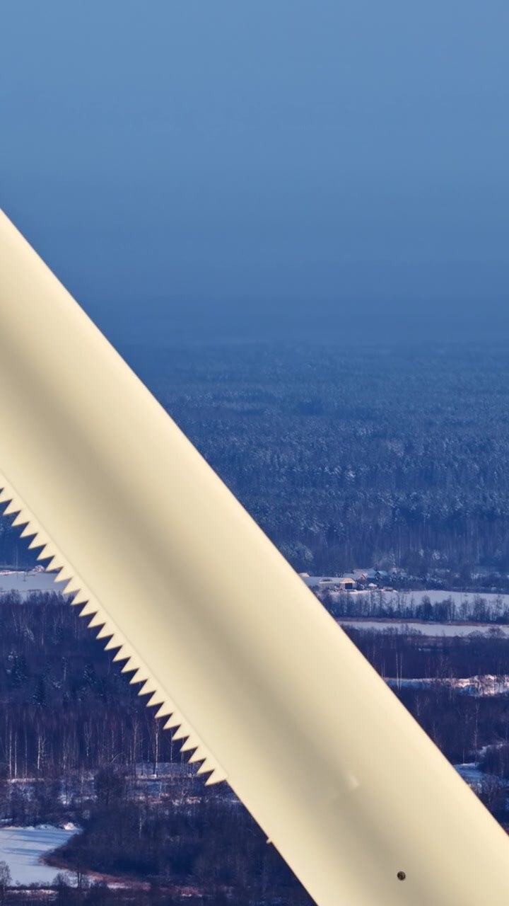 A wind turbine blade dominates the frame, set against a snowy forest landscape under a clear blue sky. Suitable for renewable energy themes or environmental documentaries.