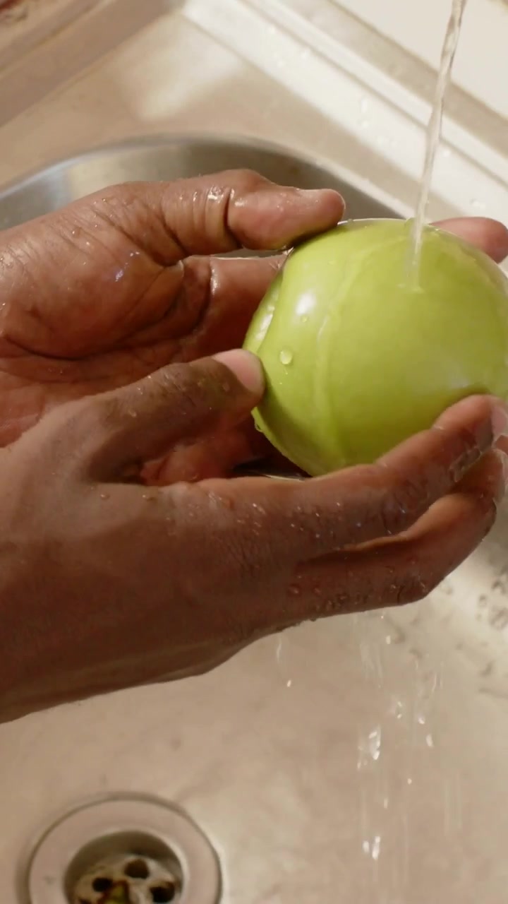 Video vertical: Hombre abriendo el grifo y enjuagando una manzana verde en el fregadero de la cocina para preparar alimentos con rábanos.