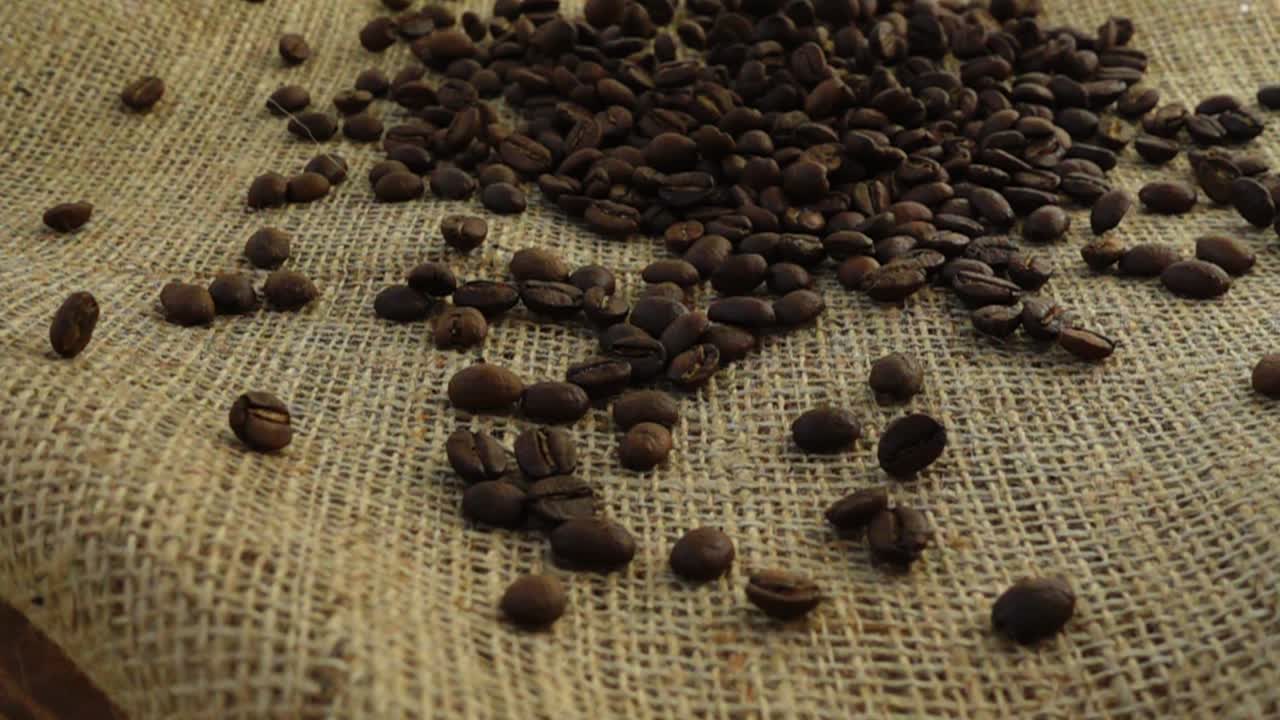 Chicchi di caffè cadono su tela di iuta al rallentatore.