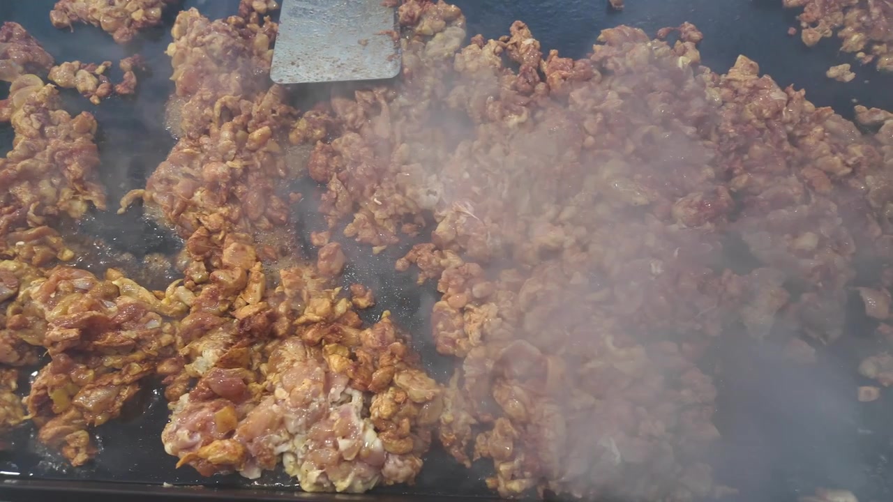 Pollo fresco condito cuoce su una piastra calda in un affollato chiosco di taco da strada mentre il vapore sale, catturando l'autentica preparazione di cibo da strada e la cultura culinaria all'aperto