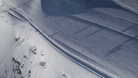 Aerial-birds-eye-shot-showing-many-skier-skiing-downhill-snow-capped-piste-in-Austria-during-sun