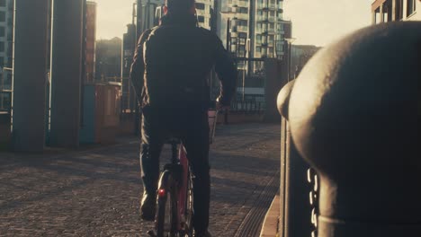 man riding bicycle in the morning, back view, city background, filmic look