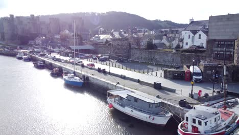 idyllic conwy castle and harbour fishing town boats on coastal waterfront aerial low angle dolly right reverse