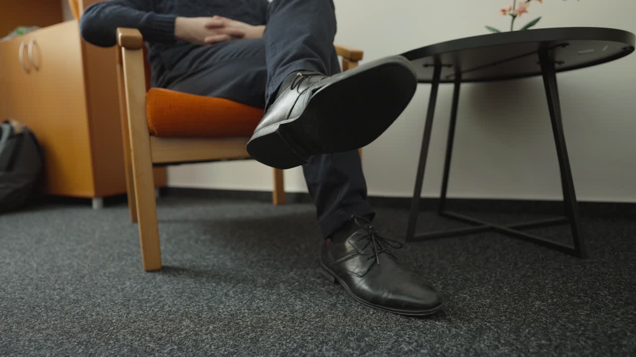 Een man tikt nerveus met zijn voet op kantoor. Stressvol werk en druk leggen druk op jongeren.