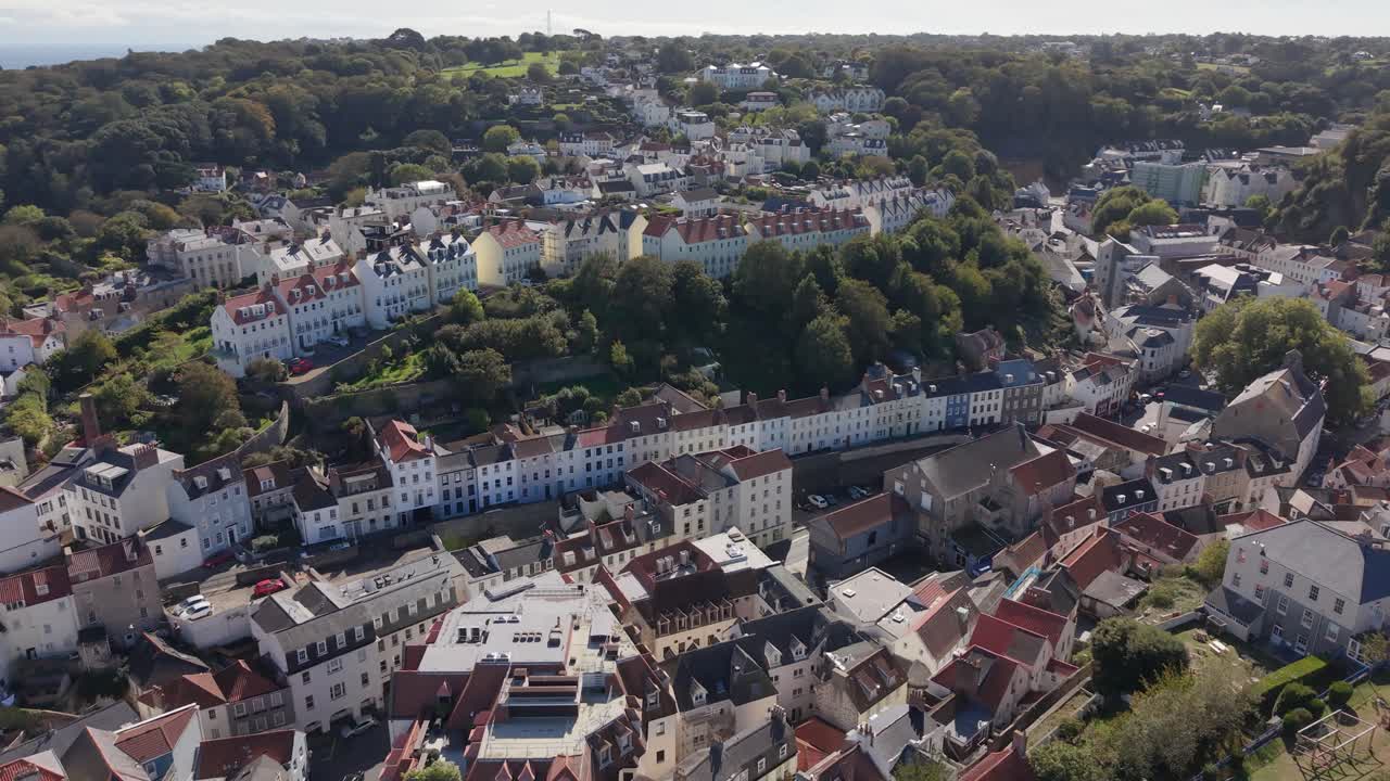 Very high drone footage over St Peter Port Guernsey showing houses and buildings rising in terraces with the land a unique perspective on a bright sunny day