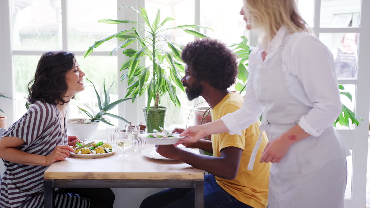 Middle aged mixed race couple eating lunch together at a table in a restaurant, a waitress brings them a side dish, close up, side view