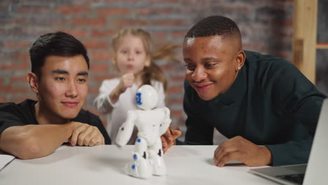 Afro-American man and Asian friend look at robot girl dances