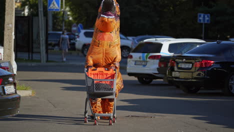 person in t-rex costume pushing shopping cart in parking lot