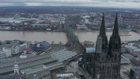 Forwards-fly-around-towers-of-Cathedral-Church-of-Saint-Peter.-High-angle-view-of-train-approaching-train-station.-Cologne,-Germany