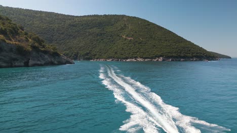 drone descends as boat skips along ocean surface in tropical island