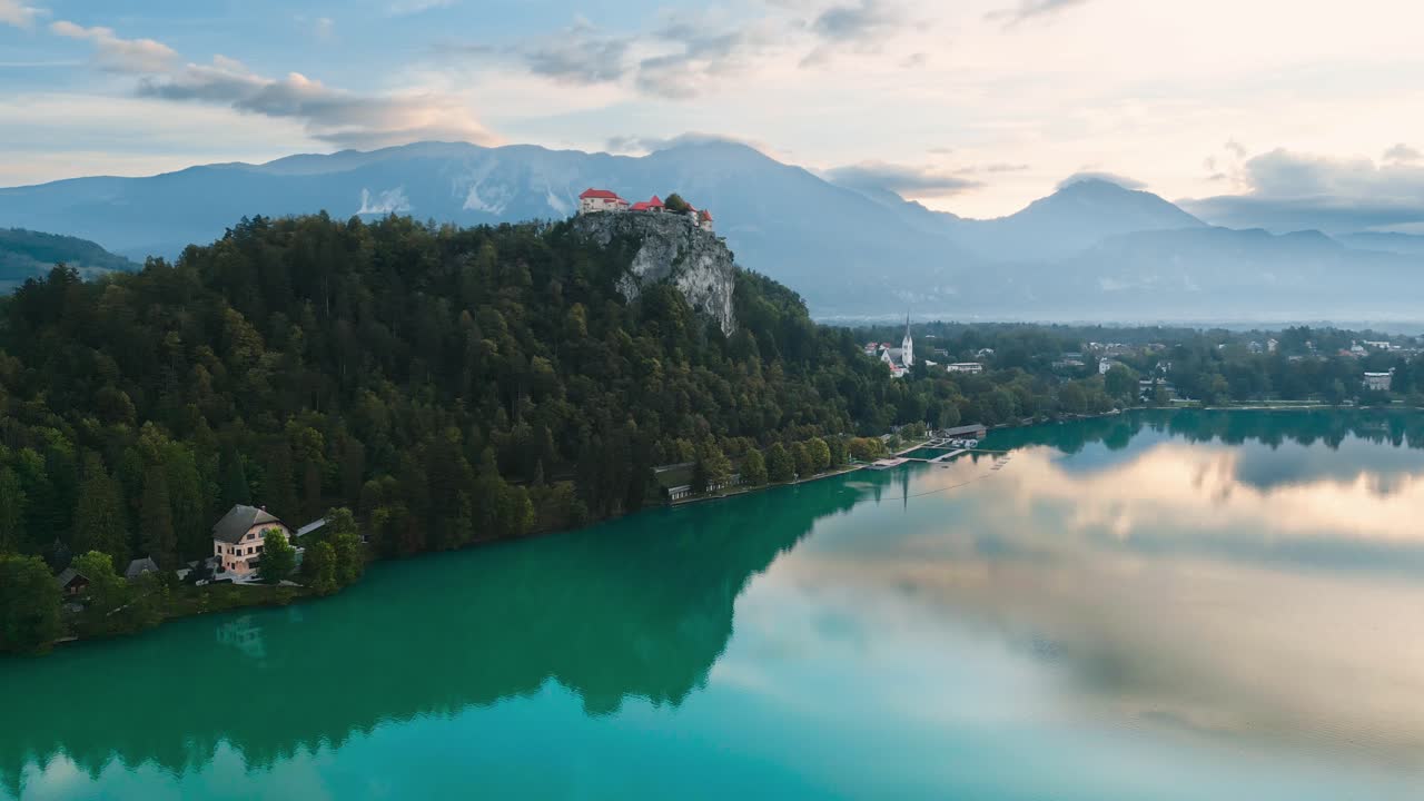 Castello di Bled su ripida scogliera rocciosa con vista sul Lago di Bled, Slovenia, con montagne sullo sfondo e riflesso, ripresa aerea con drone, splendida meta per le vacanze, primo mattino, cinematografico 4K