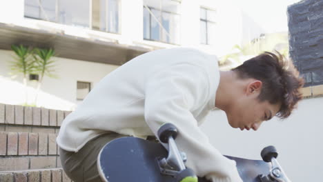 asian male teenager sitting with skateboard on sunny day in garden