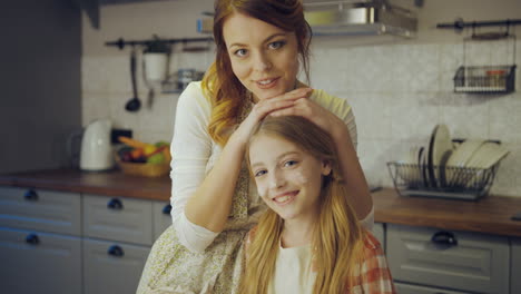 Close-up-of-the-mother-and-her-daughter-posing-in-front-of-the-camera-and-smiling-in-the-kitchen-while-cooking.-Portrait.-Indoor