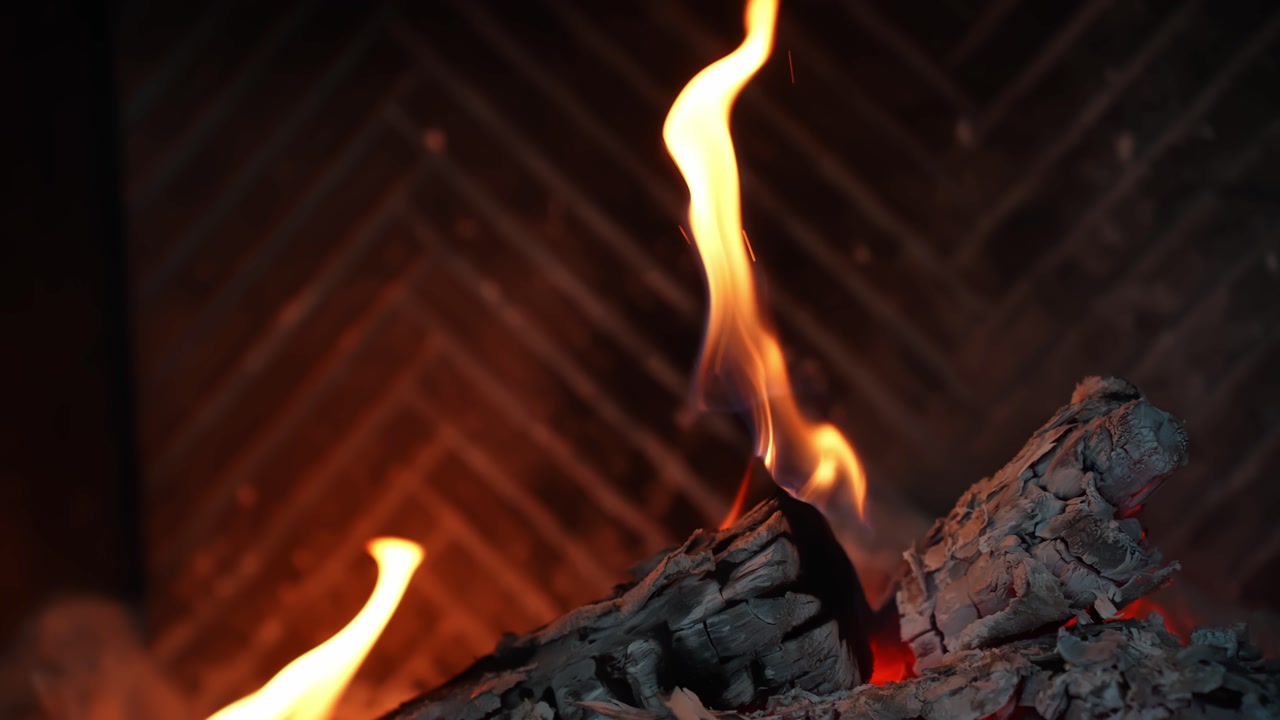 Close-up of glowing embers and flickering flames on a charred log inside a home fireplace, creating warm cozy ambience for winter heating, comfort, and relaxation.