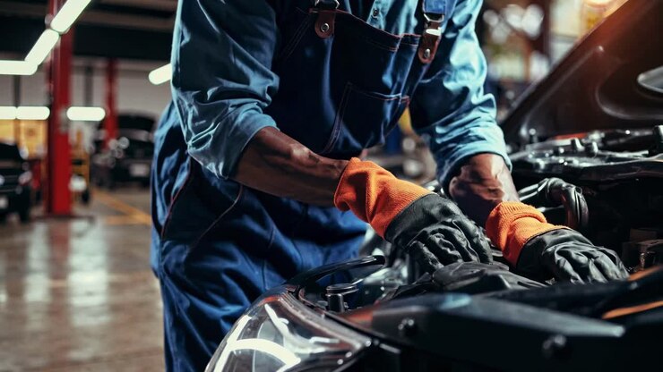Close-up video of a mechanic in blue overalls and orange gloves working on a car engine, shot