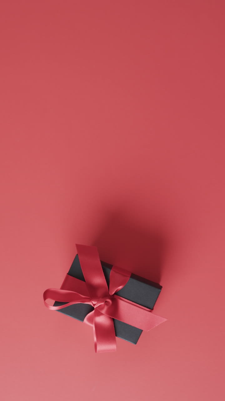 Vertical video of gift box with red ribbon and copy space over red background