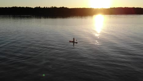 Vista-Aérea-De-Un-Hombre-Usando-Su-Paddleboard-En-Un-Lago-Durante-La-Puesta-De-Sol