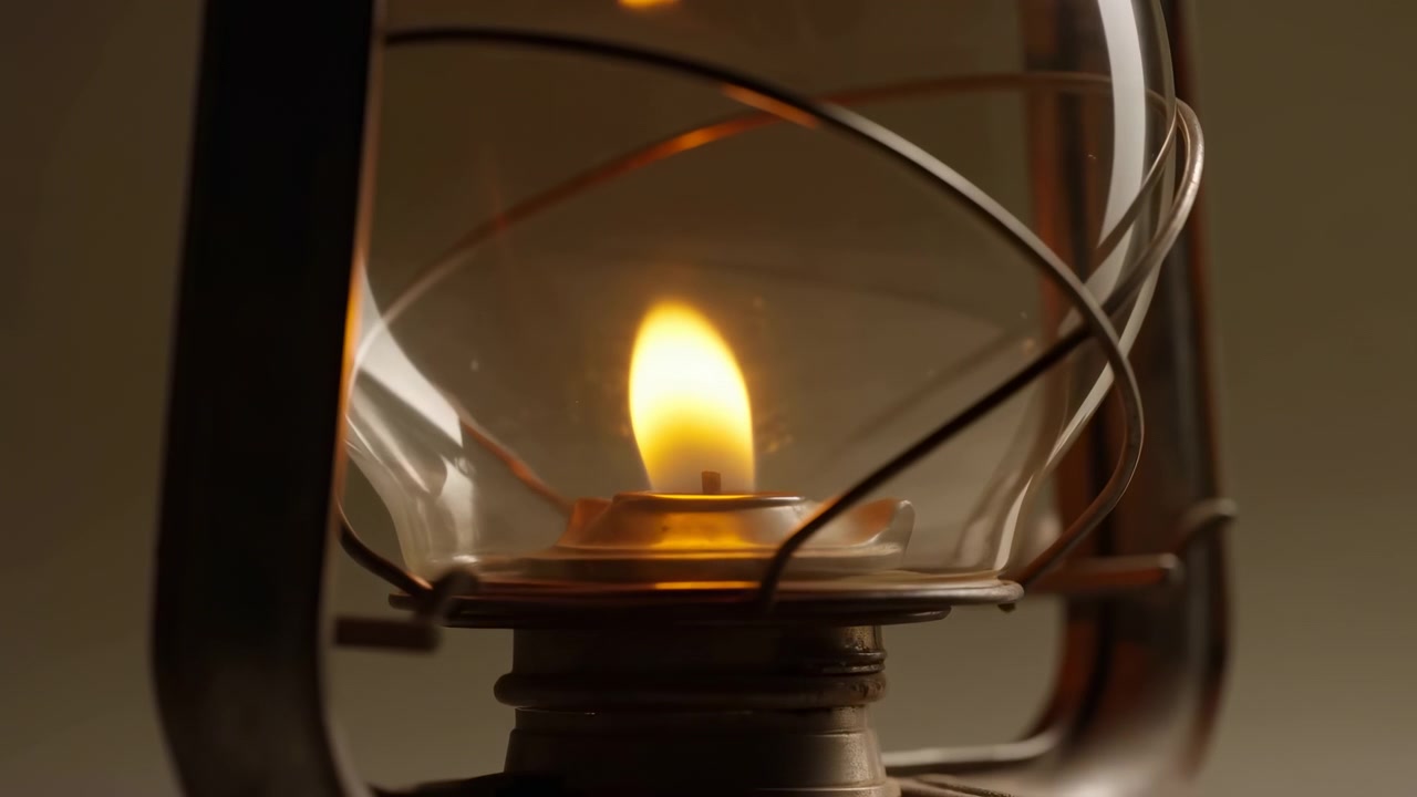 Geel-oranje vlam brandt gestaag op een metalen lontdrager in een heldere glazen schoorsteen, met gebogen donkere steundraden, zachte reflecties, een warme vintage gloed, een rustieke interieursfeer en een intieme gezellige stemming.
