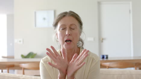 Senior woman sitting on sofa, expressing discomfort or pain at home
