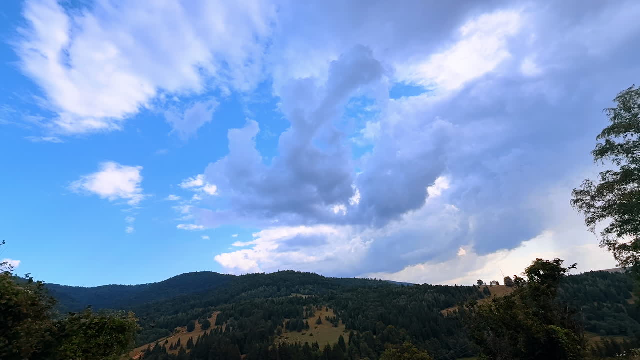 Beautiful fluffy white clouds moving in the blue sky. Aerial view on the mountains of Romania covered with green woods