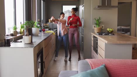 Video-of-happy-biracial-female-friends-having-fun-and-dancing-in-kitchen