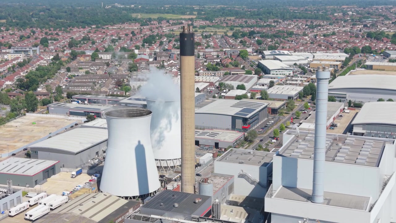 Vista aerea di una centrale elettrica multi-combustibile. Il vapore sale da un'alta ciminiera e da grandi torri di raffreddamento.