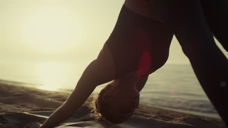 fit sportswoman bending body standing yoga asana on sandy beach close up.