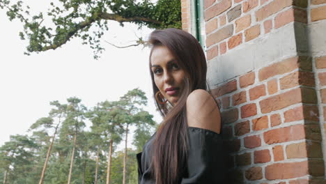 east european brunette mysteriously looking into the camera, surrounded by trees and a brick wall, slow motion footage