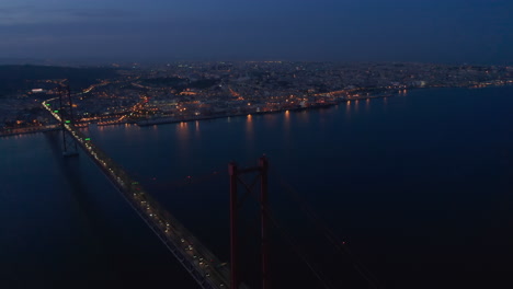 Nächtliches-Luftpanorama-Des-Städtischen-Stadtzentrums-Von-Lissabon-In-Lichtern-Mit-Der-Roten-Brücke-Ponte-25-De-Abril,-Die-Das-Meer-überquert