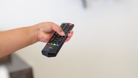 una mano presiona un botón en un control remoto en un entorno brillante y minimalista, haciendo hincapié en la interacción y la tecnología