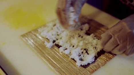 person spreading rice over green paper preparing sushi roll, homemade