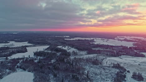 toma en ángulo alto sobre el paisaje invernal con bosque cubierto de nieve a lo largo de la carretera con un cielo amarillo brillante al amanecer en la distancia