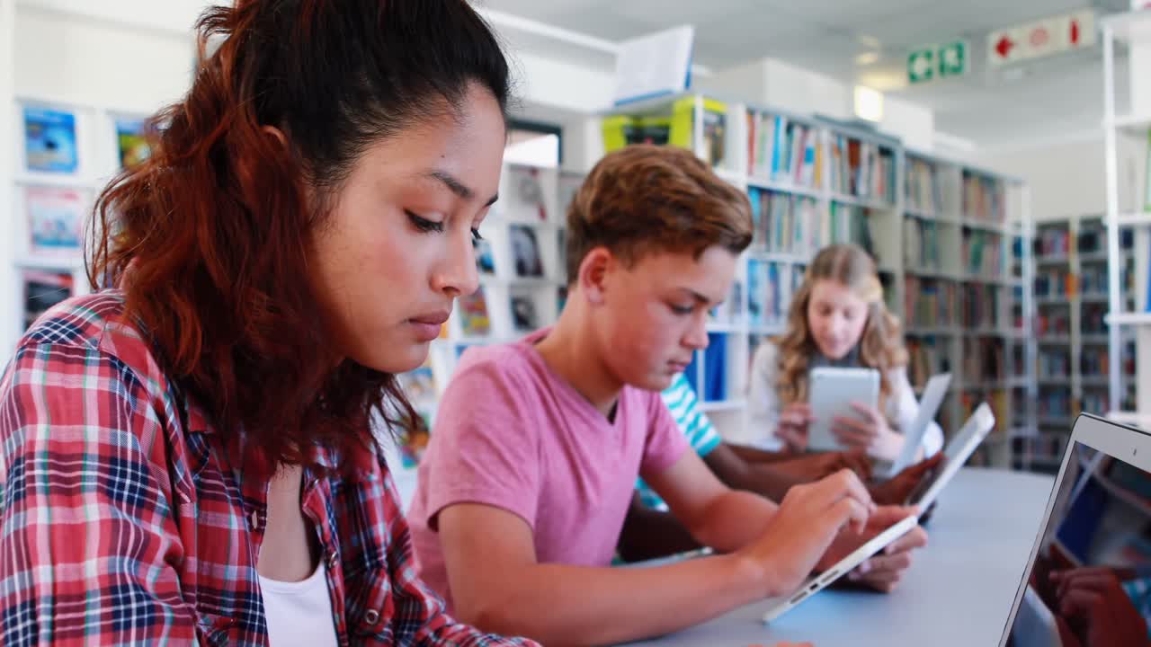 Attentive school kids using laptop and digital tablet in library