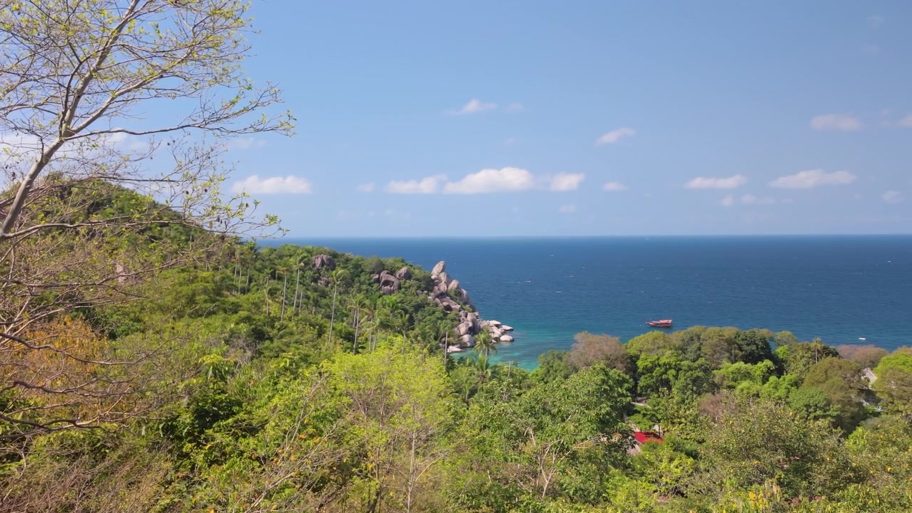 Rigogliosa collina verde che scende verso il mare blu con costa rocciosa sotto un cielo sereno, Thailandia.