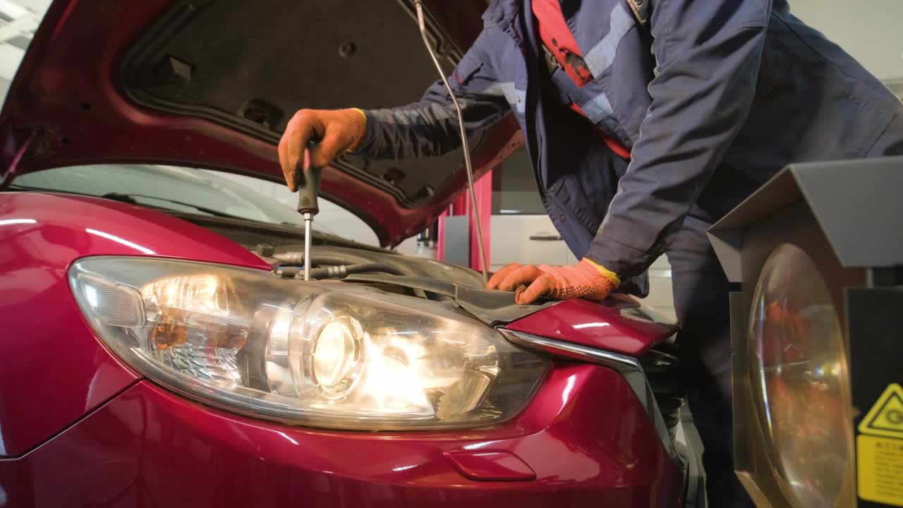 trabajador comprueba y ajusta los faros del sistema de iluminación de un automóvil. servicio de reparación de automóviles.