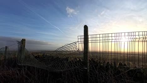 Goldene-Sonnenaufgangswolken-Im-Zeitraffer-über-Verdrehtem,-Metallenem-Ackerland-Und-Eingezäunter-Morgenwiese