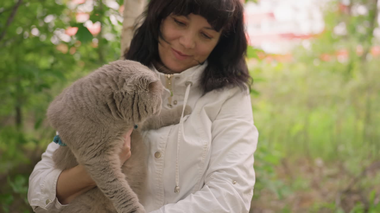Man Embraces Cat Outside, Person Holding Gray Cat In Park, Man Cuddles Fluffy Gray Cat In Peaceful Outdoor Setting, Male Owner Warmly Embraces His Soft Furred Pet Amid Lush Green Scenery