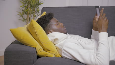 portrait of concentrated man lying on couch using digital tablet