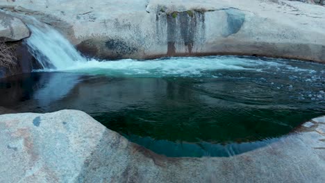 toma panorámica hacia la derecha de una cascada que desemboca en una piscina profunda que se derrama sobre una resbaladiza roca de granito.