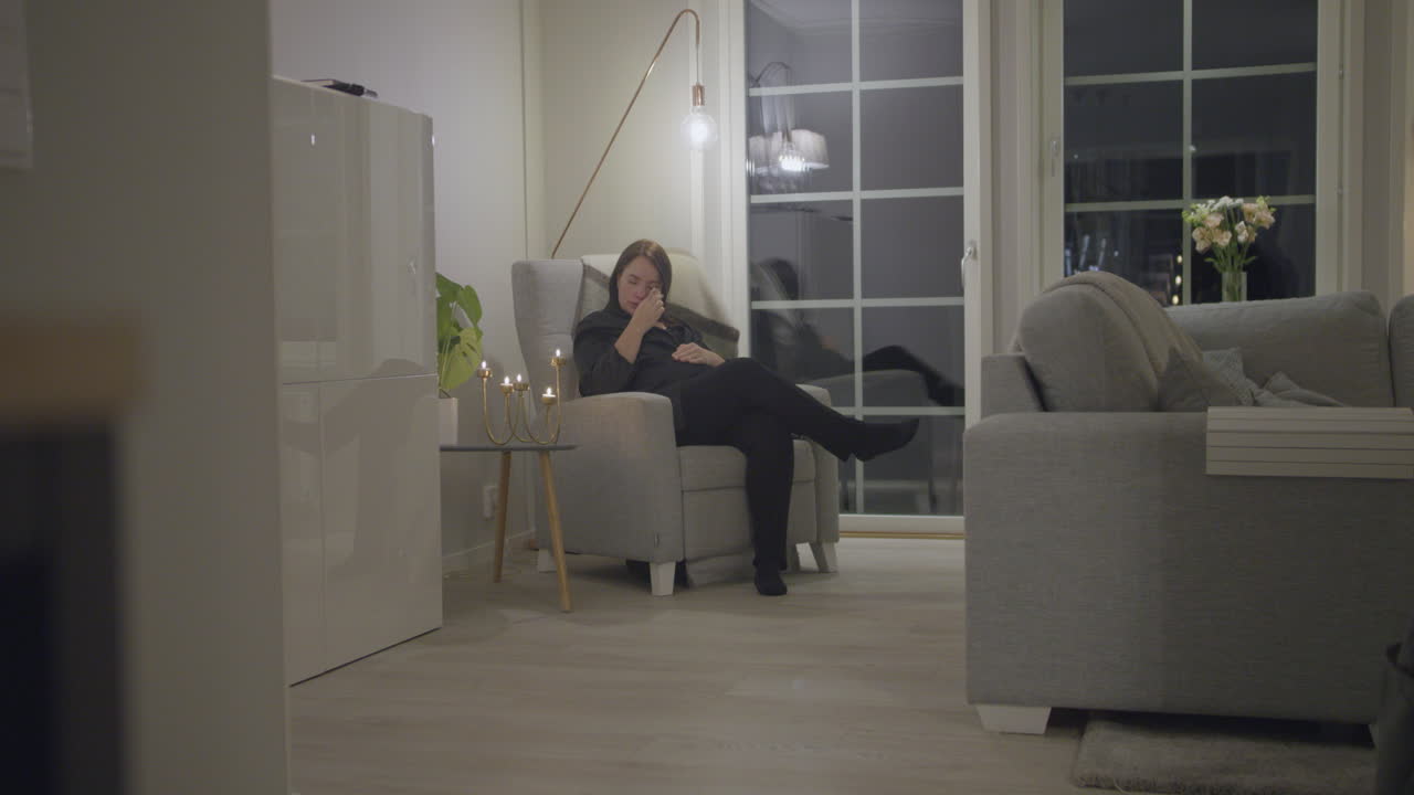 de la comodidad del hogar - mujer adulta llorando en la silla de la sala de estar, secando las lágrimas de los ojos