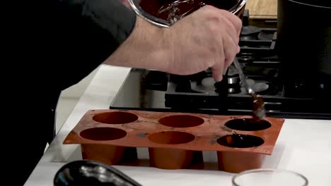 in a modern kitchen, a chef skillfully pours melted chocolate into a silicone mold using a brush. the process showcases precision and artistry, focusing on dessert preparation
