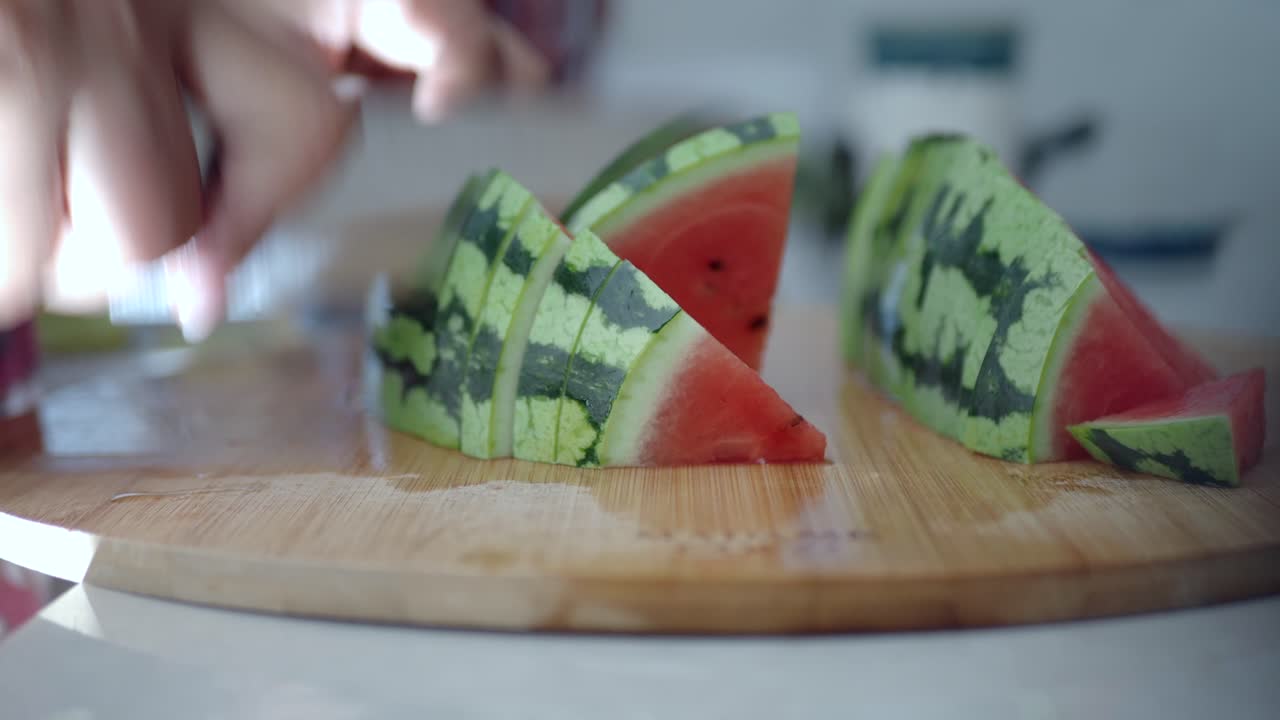 Hands slicing fresh watermelon on a wooden cutting board