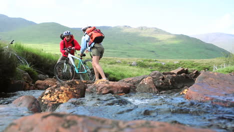 couple crossing a stream together with their bikes