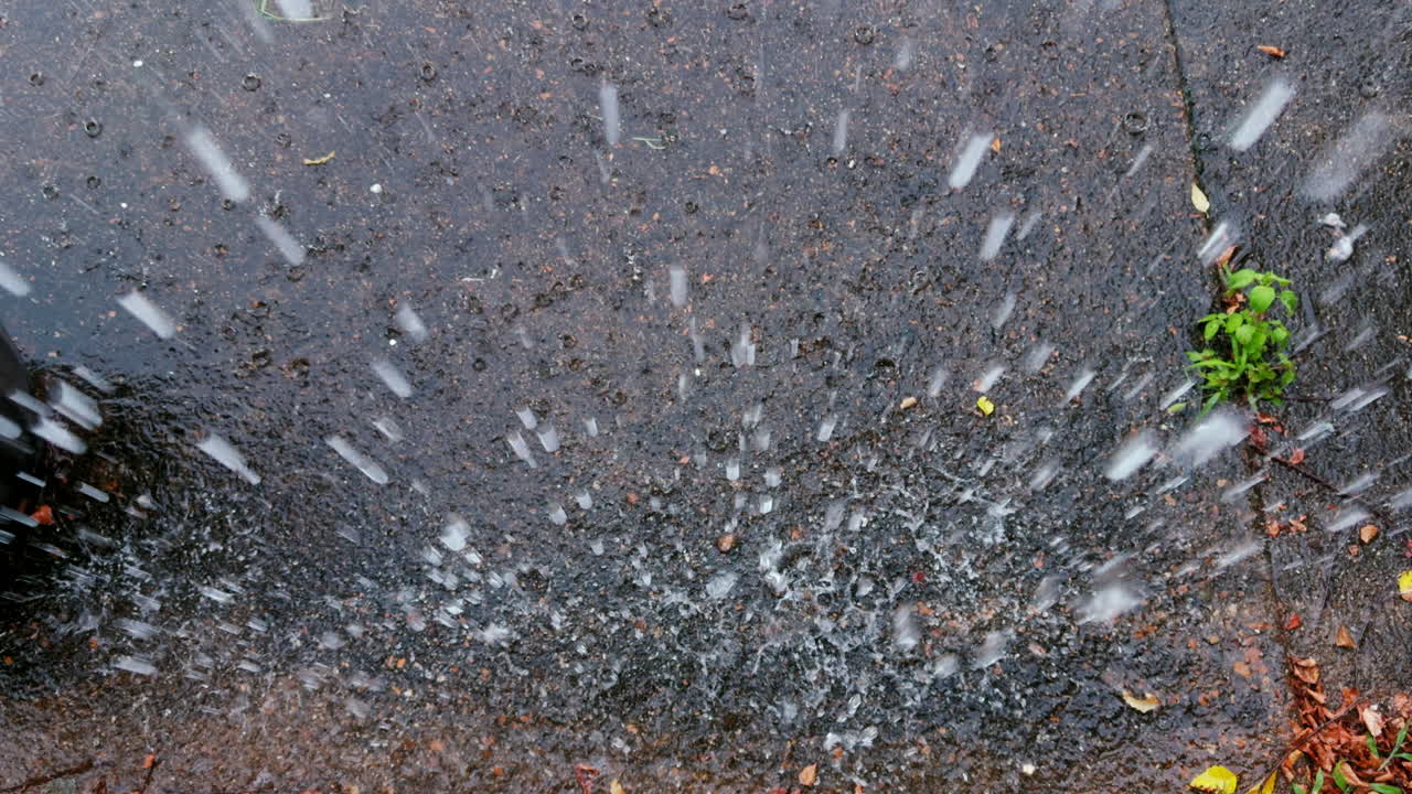 Slow motion footage of rainddrops from the gutter of a house hitting the concrete of a driveway during a heavy storm